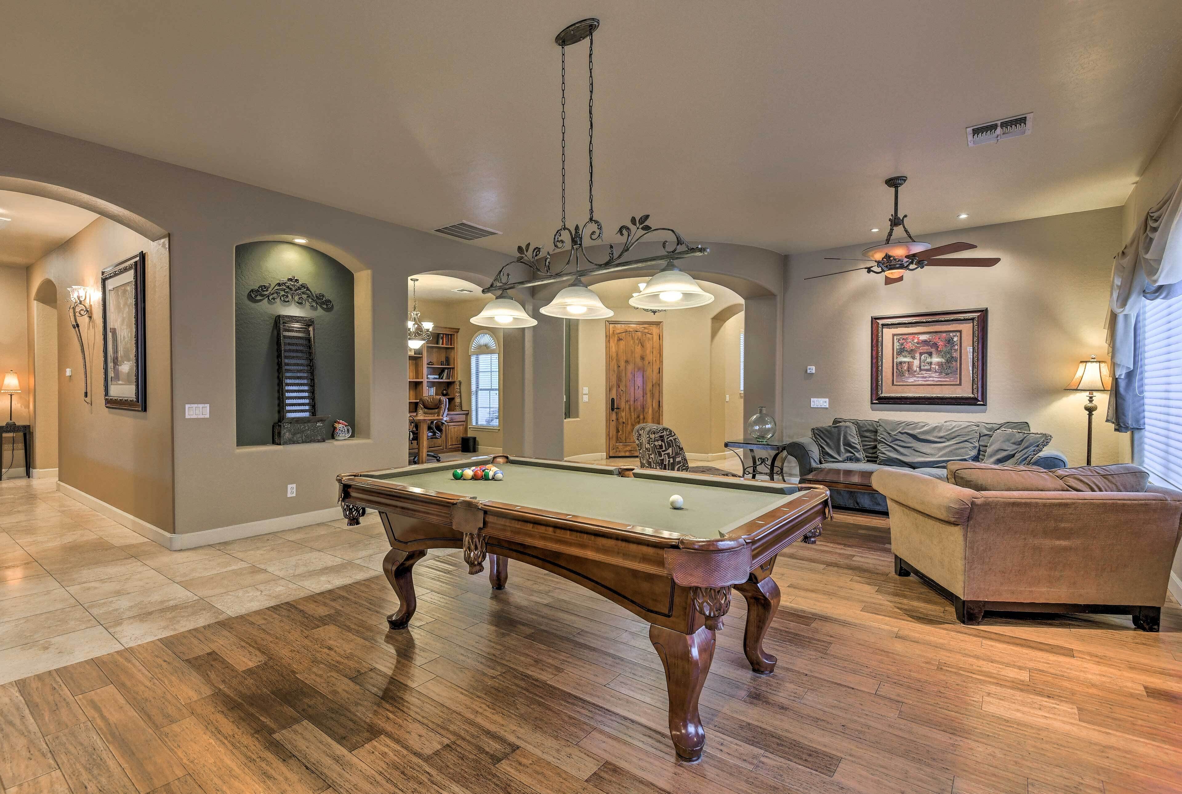 Un vaste espace de vie comprenant une table de billard, un ventilateur de plafond et un coin salon confortable.