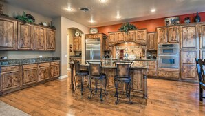 A spacious kitchen with wooden cabinets, a central island with bar stools, stainless steel appliances, and a tiled backsplash. - Heated Pool + Putting Green: Luxe Gilbert Home (Gilbert)