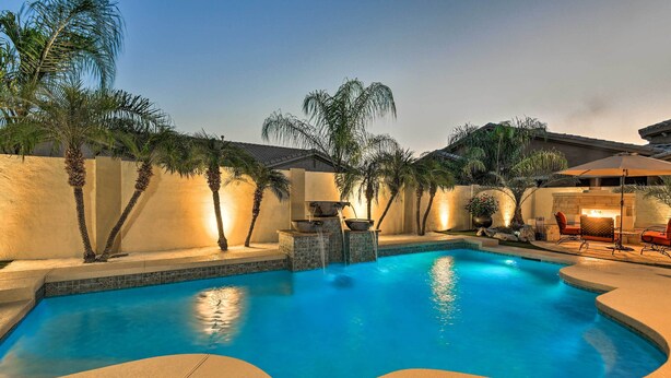 A swimming pool with a curved edge, surrounded by palm trees and a stone wall. - Heated Pool + Putting Green: Luxe Gilbert Home (Gilbert)