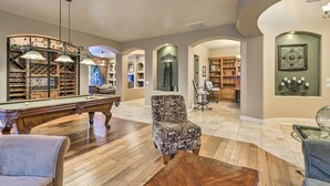A spacious living room with a pool table, a patterned armchair, and a ceiling fan. - Heated Pool + Putting Green: Luxe Gilbert Home (Gilbert)