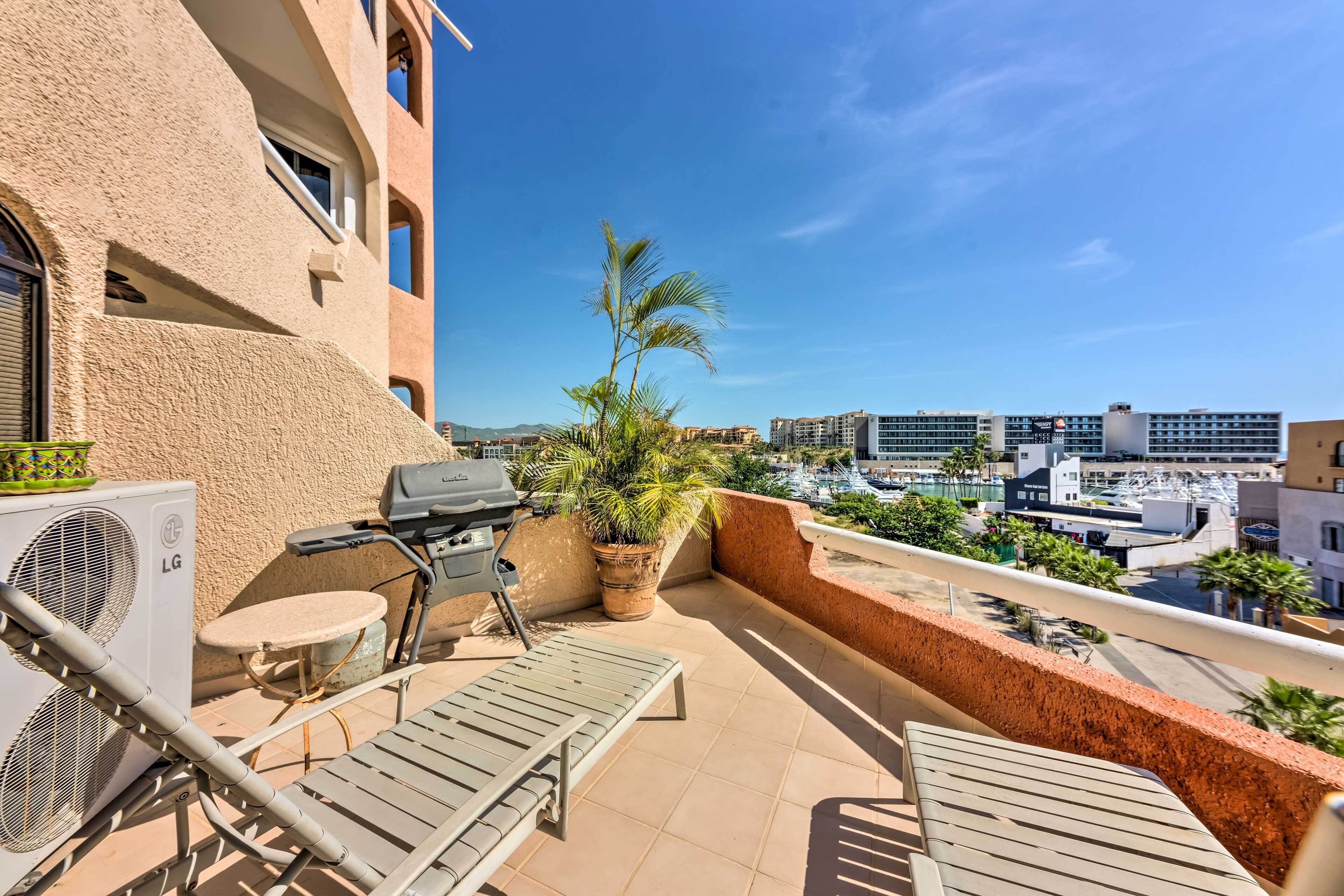 A balcony with a grill, lounge chairs, and a potted plant.