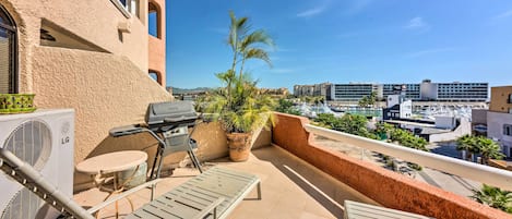 A balcony with a grill, lounge chairs, and a potted plant.