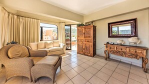 Sala de estar com sofá bege, poltronas de vime, um armário de madeira e uma janela grande com cortinas.