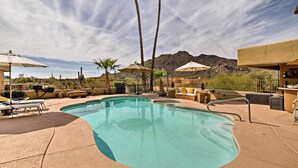 A swimming pool with lounge chairs and umbrellas, surrounded by palm trees and desert plants, with mountains in the background. - Cozy Casita w/ Mtn View + Pool & Hot Tub Access (Carefree)