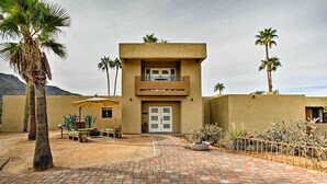 A two-story building with a flat roof, a balcony on the upper floor, and a paved courtyard with palm trees and cacti. - Cozy Casita w/ Mtn View + Pool & Hot Tub Access (Carefree)