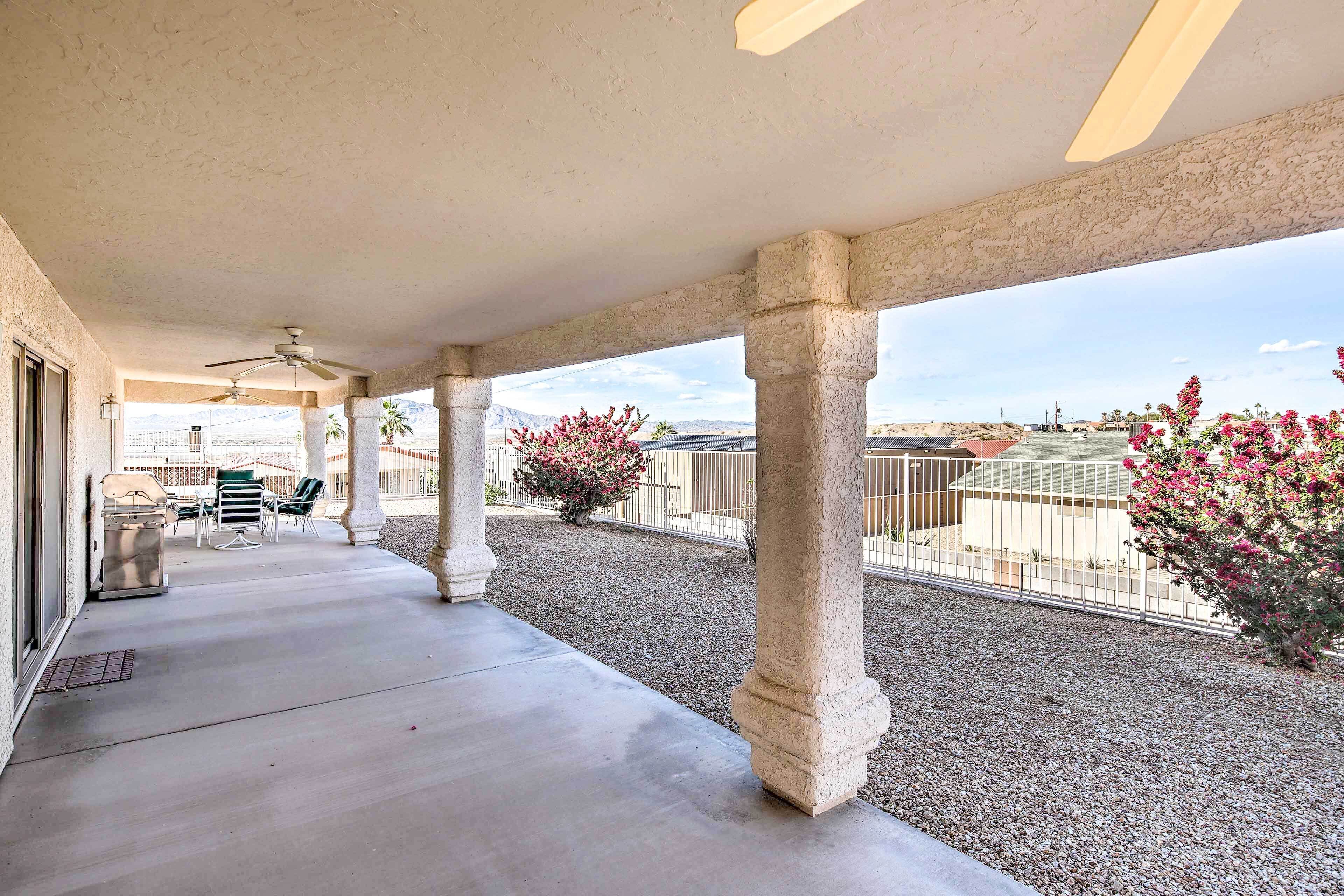 A covered patio area with a concrete floor, stone columns, ceiling fans, and a view of the surrounding landscape.