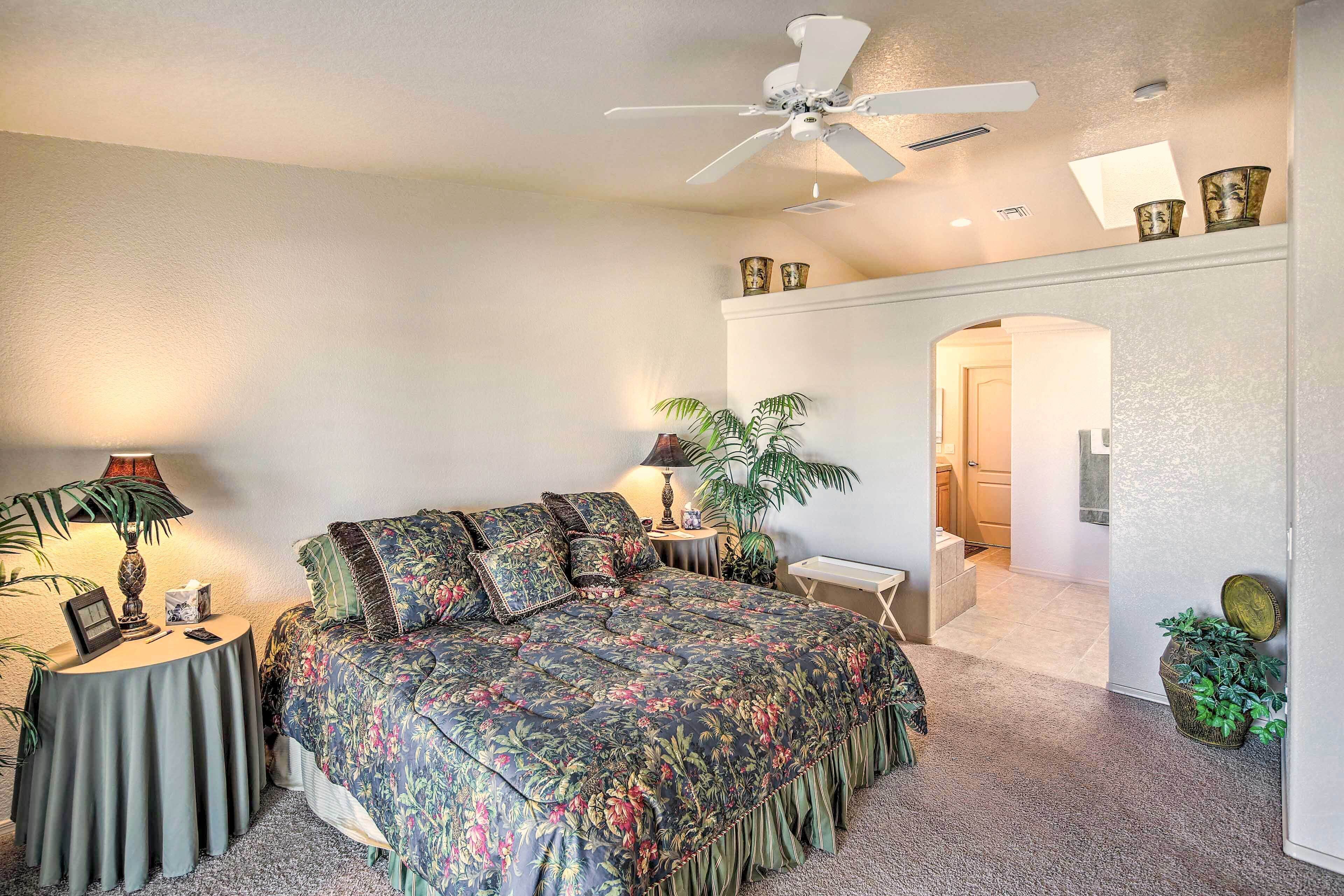 A bedroom with a bed, a ceiling fan, a nightstand with a lamp, and a potted plant.