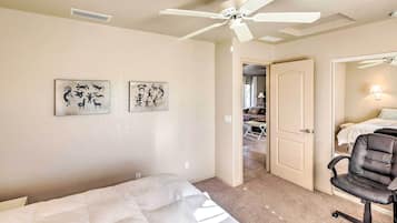 Habitación de hotel con cama, escritorio, silla, ventilador de techo y dos obras de arte en la pared.