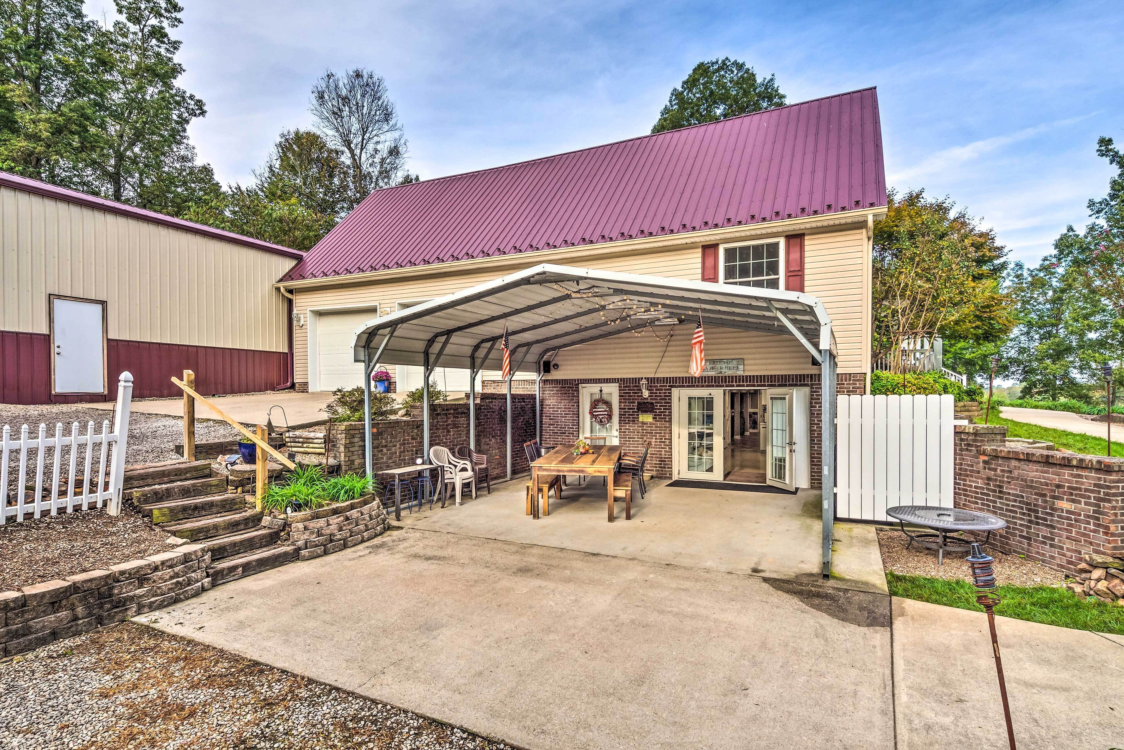A covered patio area with a table and chairs, a small garden, and a building with a red roof.
