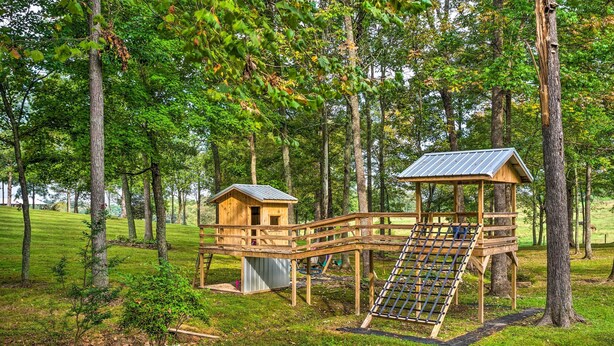 A wooden play structure with a slide and a small house, surrounded by trees and grass. - Mammoth Cave Rental on 50 Acres: Shared Amenities (Mammoth Cave)
