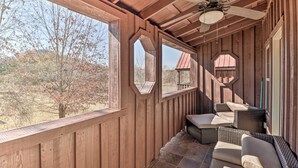 Ein überdachter Außenbereich mit Holzwänden, einem Deckenventilator und Blick auf Bäume und ein Gebäude im Hintergrund.