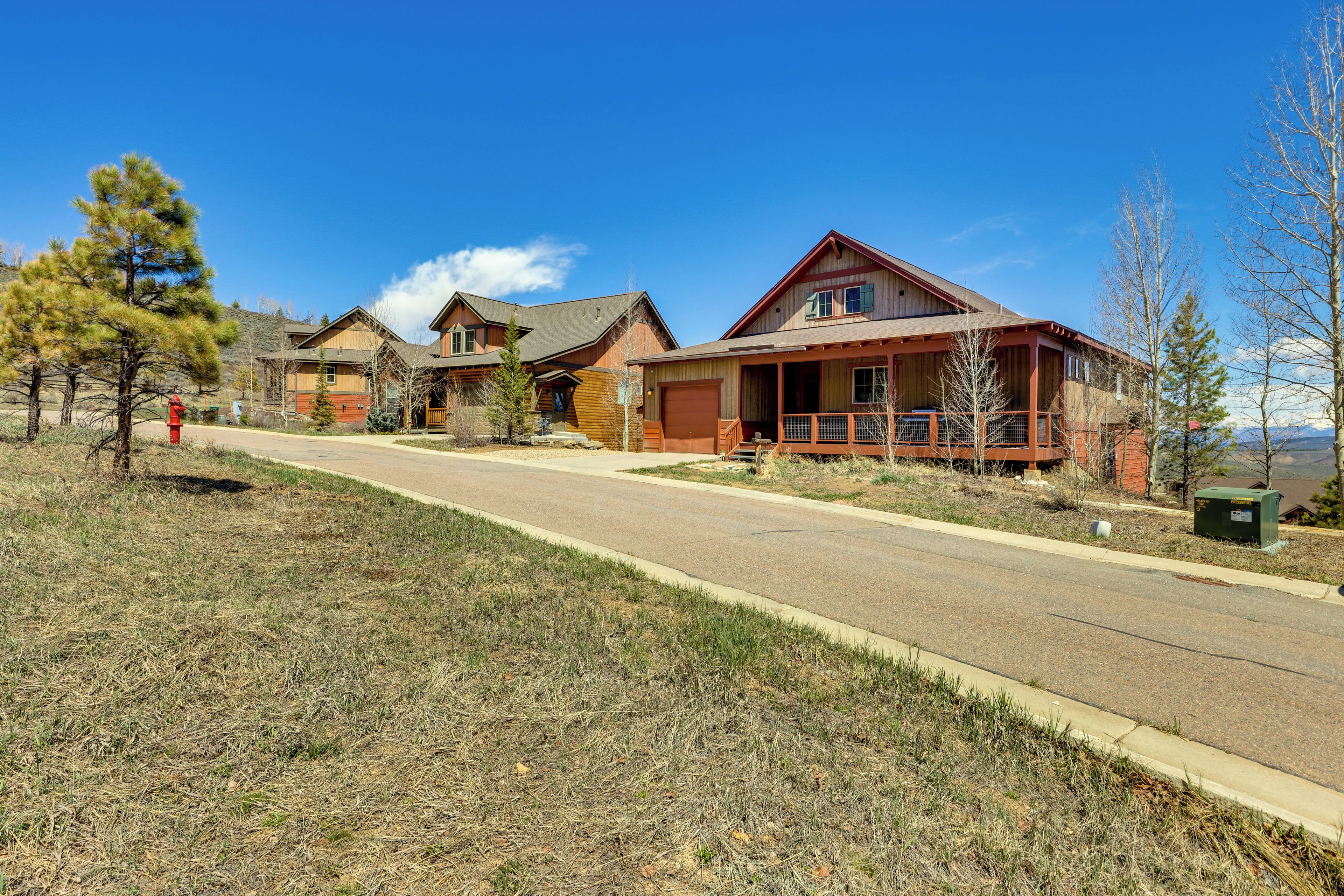 A row of wooden houses with a clear road in front, surrounded by sparse grass and a few trees.