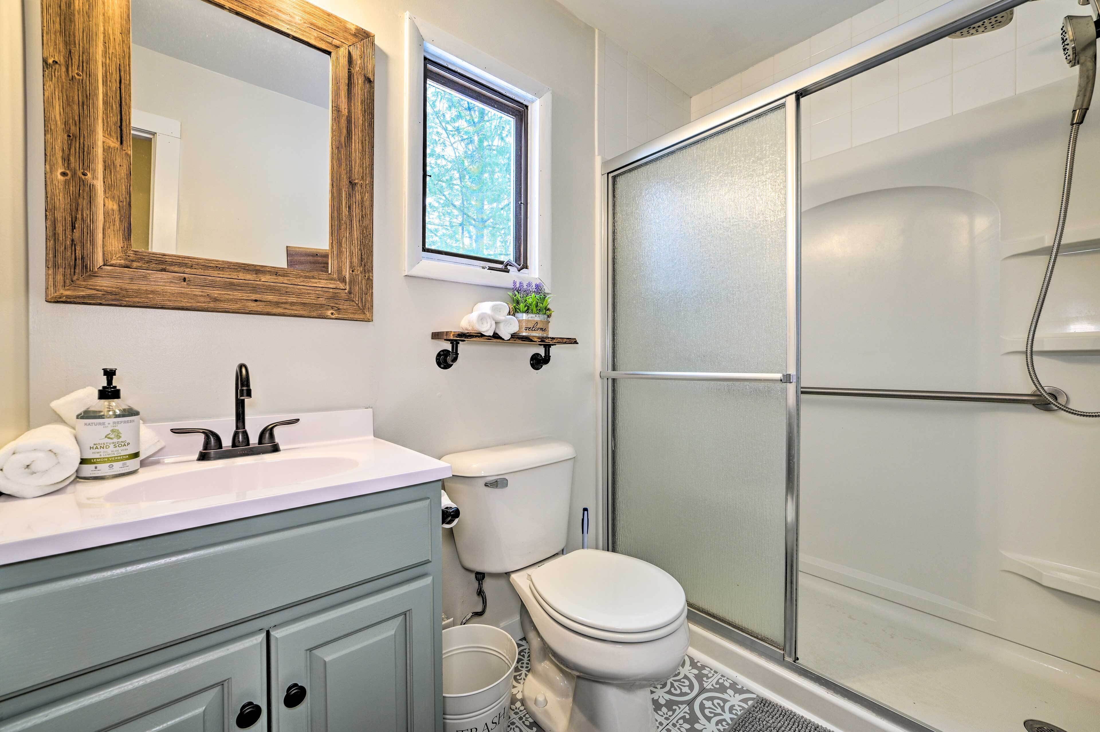 Un baño con un lavamanos blanco, un inodoro, una ducha con puerta de cristal y una ventana con vistas a árboles.
