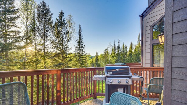 Eine Terrasse mit Grill, Stühlen und Blick auf einen Wald.
