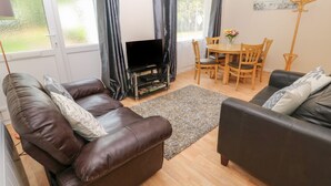 Un salon avec deux canapés, un téléviseur, une table à manger avec des chaises et un tableau accroché au mur.