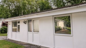 Une maison blanche d’un seul étage, avec une grande fenêtre sur le côté droit, une porte et un petit porche.