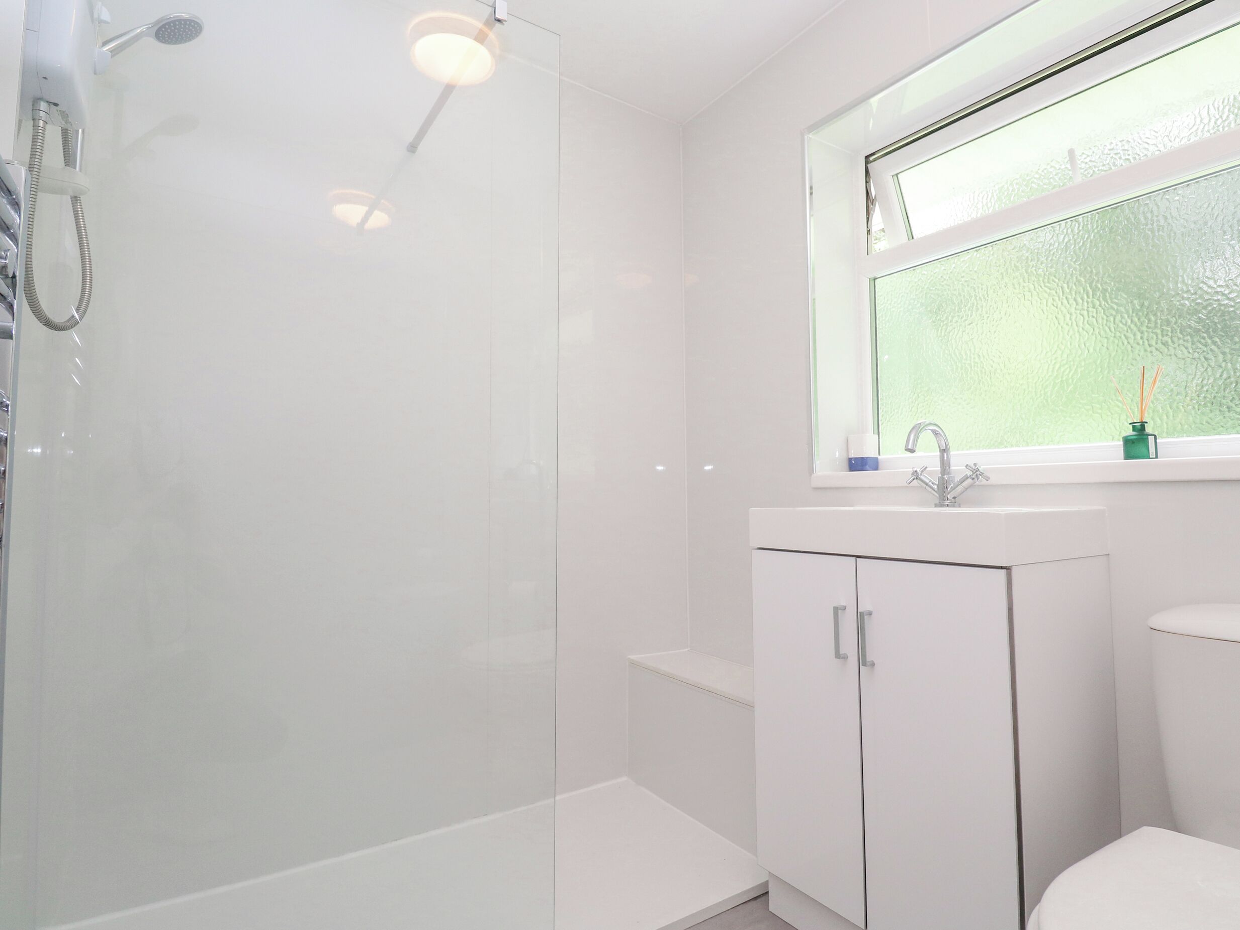 Un baño moderno con cabina de ducha de vidrio, un lavamanos blanco y una ventana con vista a través de vidrio esmerilado.