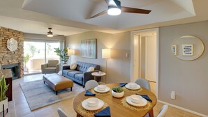 A modern living room with a fireplace, a dining area with a round table set for four, and a cozy seating area with a sofa and armchairs. - First-floor Condo w/ Golf Course Views & Pool! (Scottsdale)