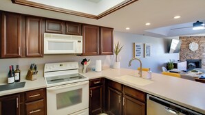 A modern kitchen with dark wooden cabinets, a white stove, and a large window above the countertop. - First-floor Condo w/ Golf Course Views & Pool! (Scottsdale)