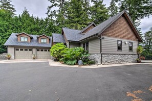 A two-story house with a garage, surrounded by lush greenery and a stone wall.