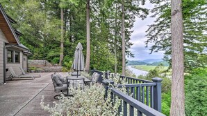Eine Terrasse mit Gartenmöbeln, Blick auf einen Fluss und hohe Bäume.