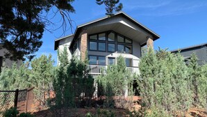 A two-story house with a balcony, surrounded by trees and a fenced area. - Mountain View Modern Cabin: Luxury Pine Home! (Pine)
