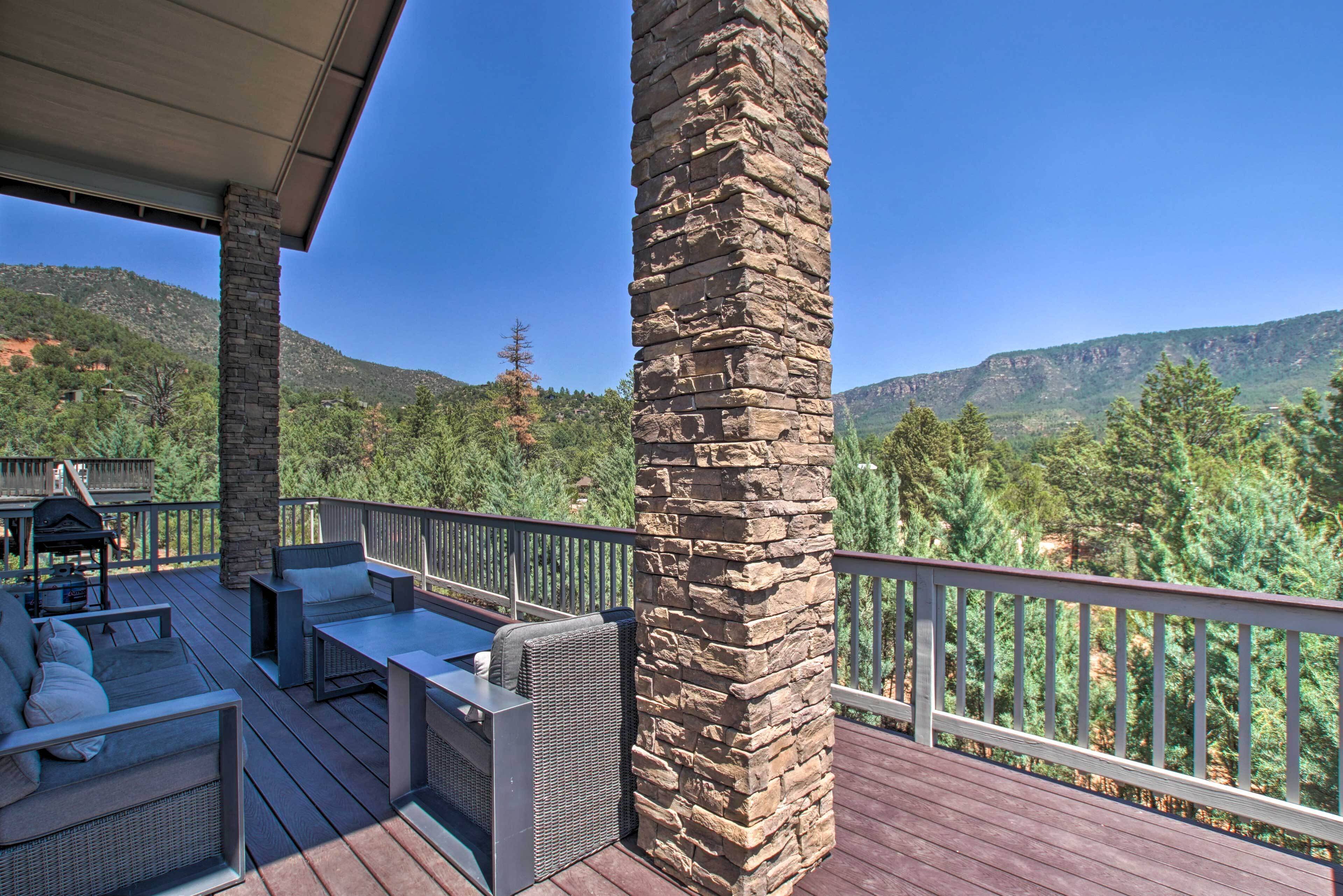 A wooden deck with outdoor furniture, stone pillars, and a view of a mountainous landscape.