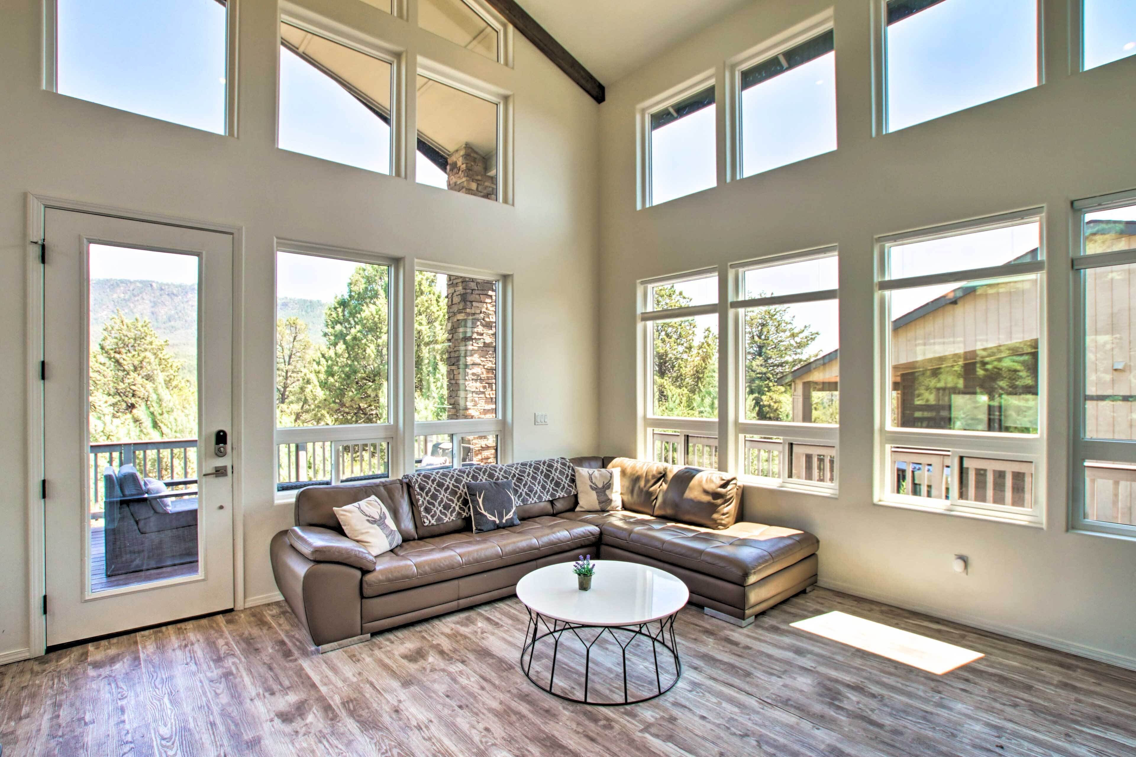 A spacious living room with a large sectional sofa, a round coffee table, and multiple windows offering views of the outdoors.