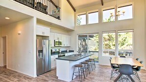 A spacious kitchen with a large island, stainless steel appliances, and a dining area with a long table and bar stools. - Mountain View Modern Cabin: Luxury Pine Home! (Pine)