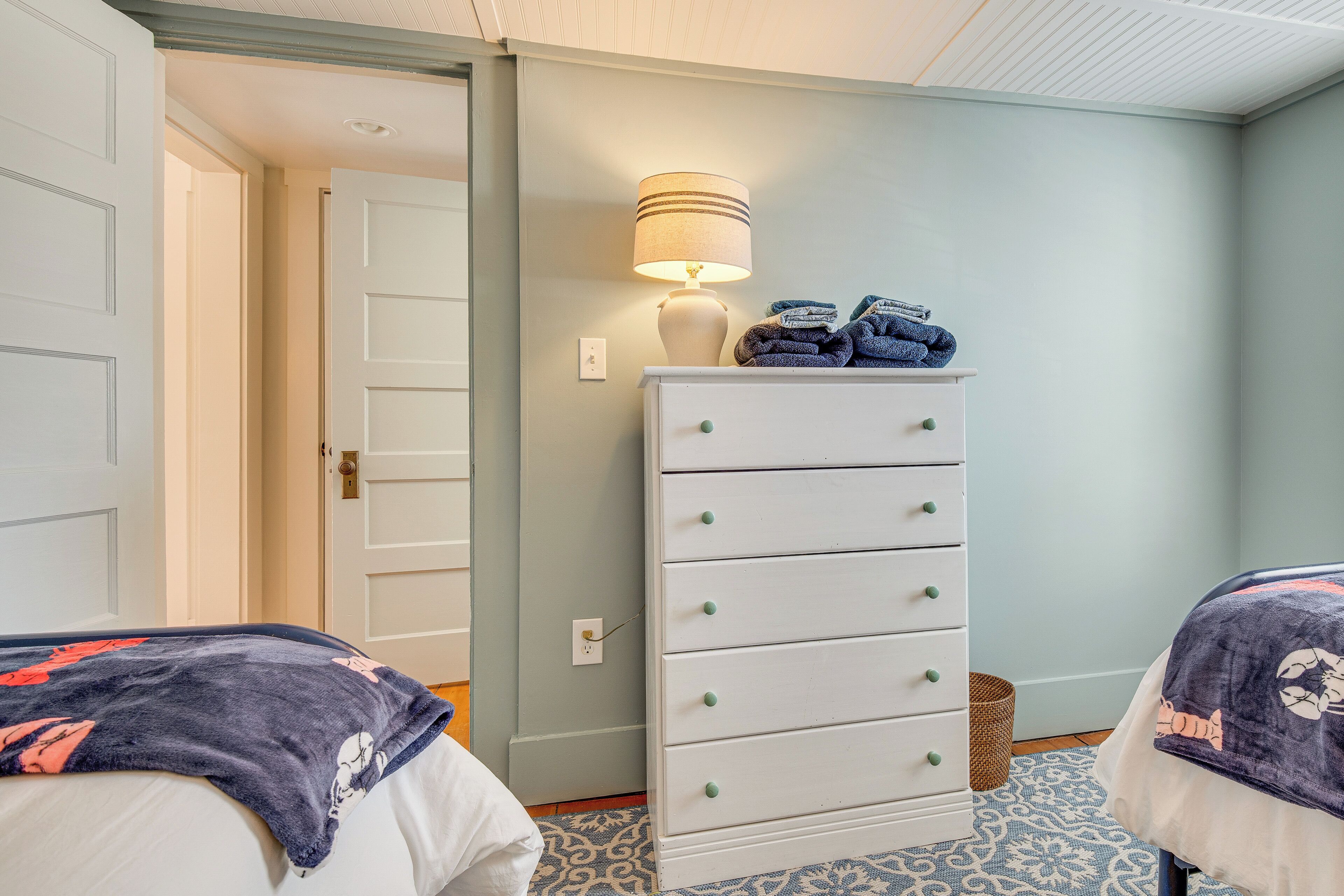 A bedroom with two beds, a dresser, a lamp, and a patterned rug.