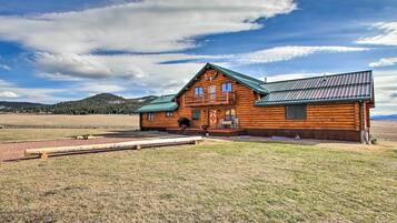 A log cabin with a balcony, a green roof, and a view of a field and mountains in the background.