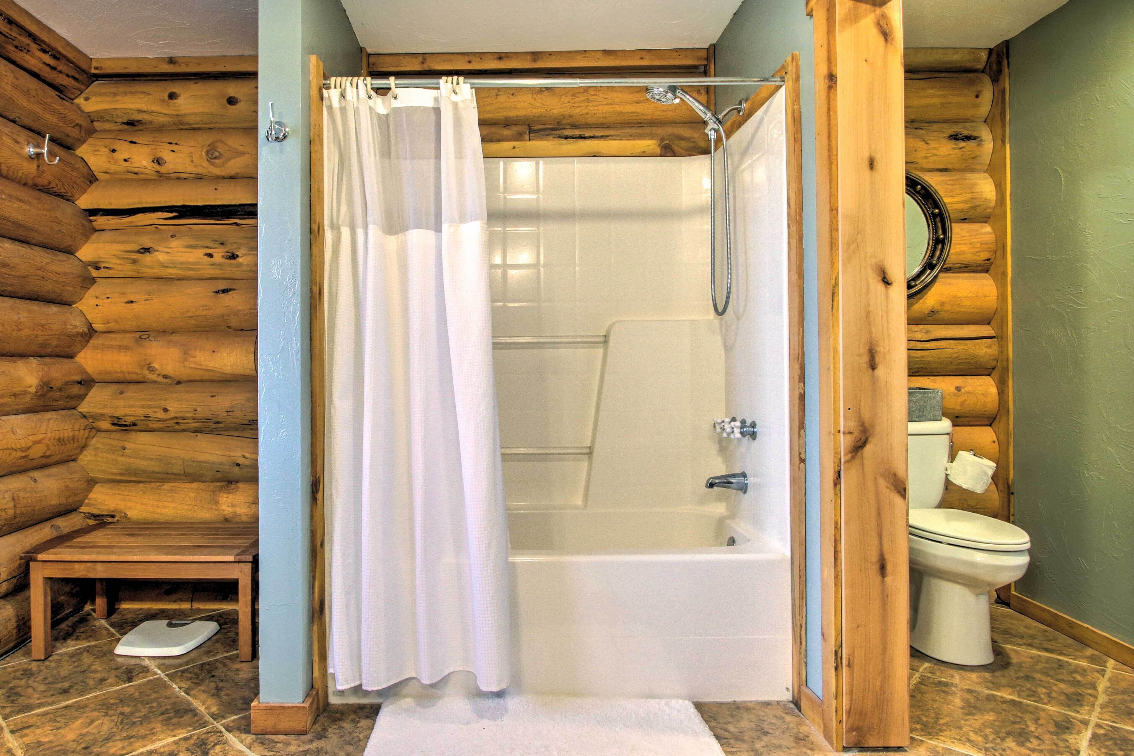 Une salle de bain rustique, aménagée dans une cabane en bois, avec une douche, des toilettes et une petite table en bois sur laquelle se trouve une balance.