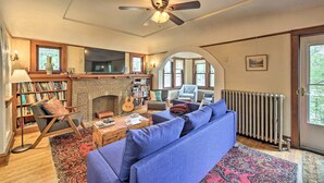 A cozy living room with a fireplace, bookshelves, a blue sofa, and a ceiling fan.