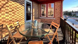 A glass table with chairs on a balcony with a brick wall and a red roof.