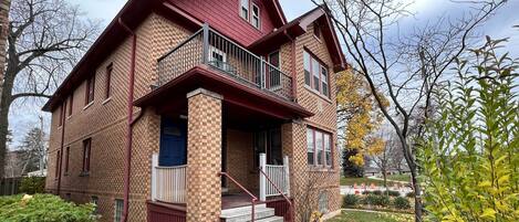 A two-story brick house with a red roof, a front porch, and a small front yard.