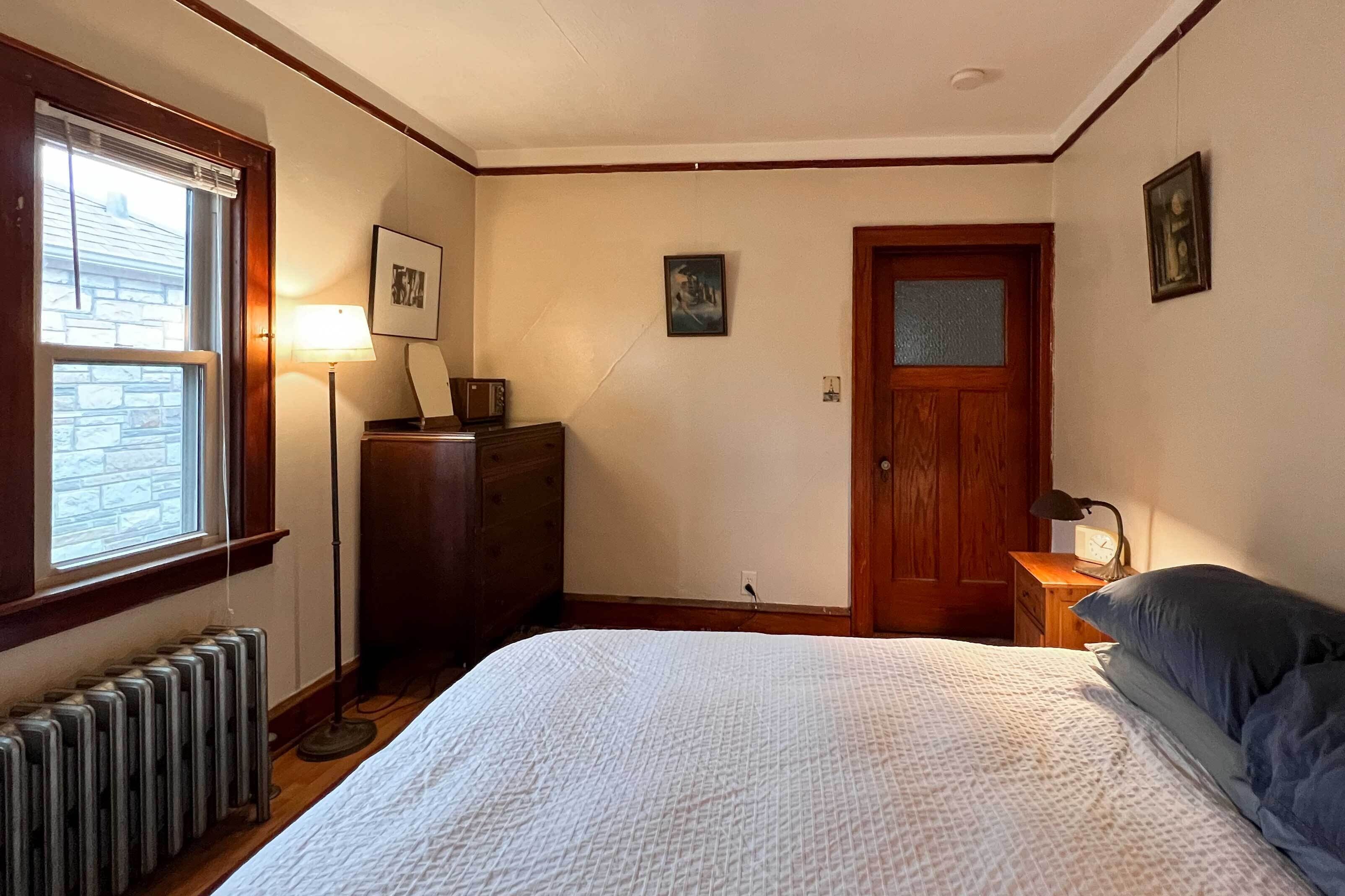 A bedroom with a bed, a dresser, a nightstand, a window, and a door.