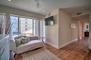 A modern living room with a sofa, a small side table, and a large window with curtains. - Family-friendly Brigantine Condo Near Beach! (Brigantine)
