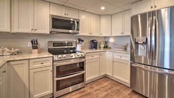 Una cocina moderna con gabinetes blancos, electrodomésticos de acero inoxidable, microondas, estufa, horno y refrigerador.