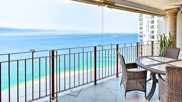 A balcony with a view of the ocean, a round table with chairs, and a railing. - Beachfront Resort Condo w/ Wraparound Balcony! (Puerto Vallarta)