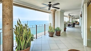 A spacious balcony with a view of the ocean, potted plants, and ceiling fans. - Beachfront Resort Condo w/ Wraparound Balcony! (Puerto Vallarta)