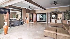 A spacious living area with a high ceiling, a ceiling fan, a large mirror, and a seating area with a sofa and ottomans. - Beachfront Resort Condo w/ Wraparound Balcony! (Puerto Vallarta)