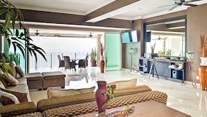 A spacious living area with a balcony, modern furniture, and a television. - Beachfront Resort Condo w/ Wraparound Balcony! (Puerto Vallarta)