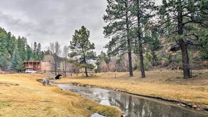 Una cabaña rodeada de bosque con un arroyo que la atraviesa.