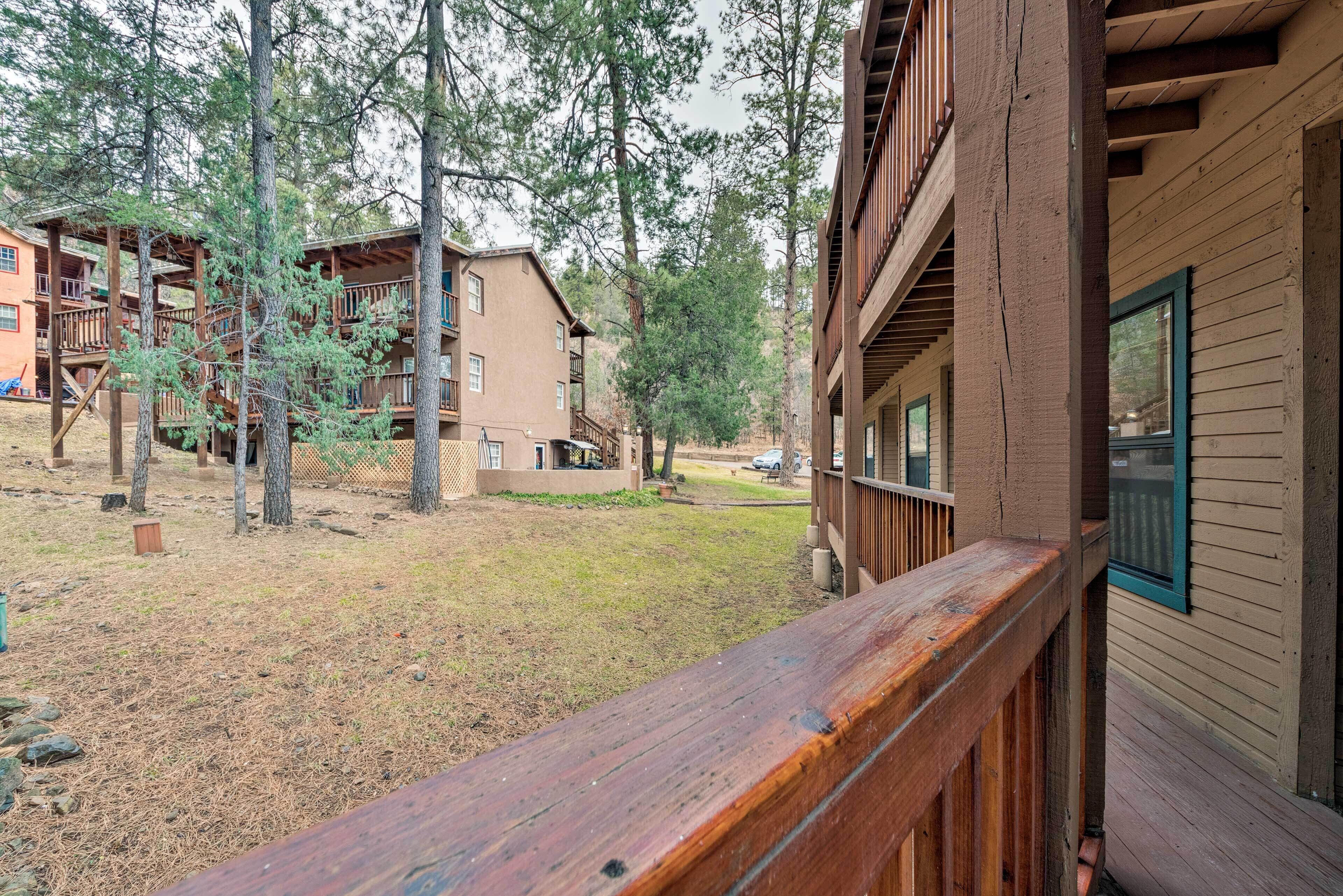 A wooden cabin with a balcony, surrounded by trees and a grassy area.