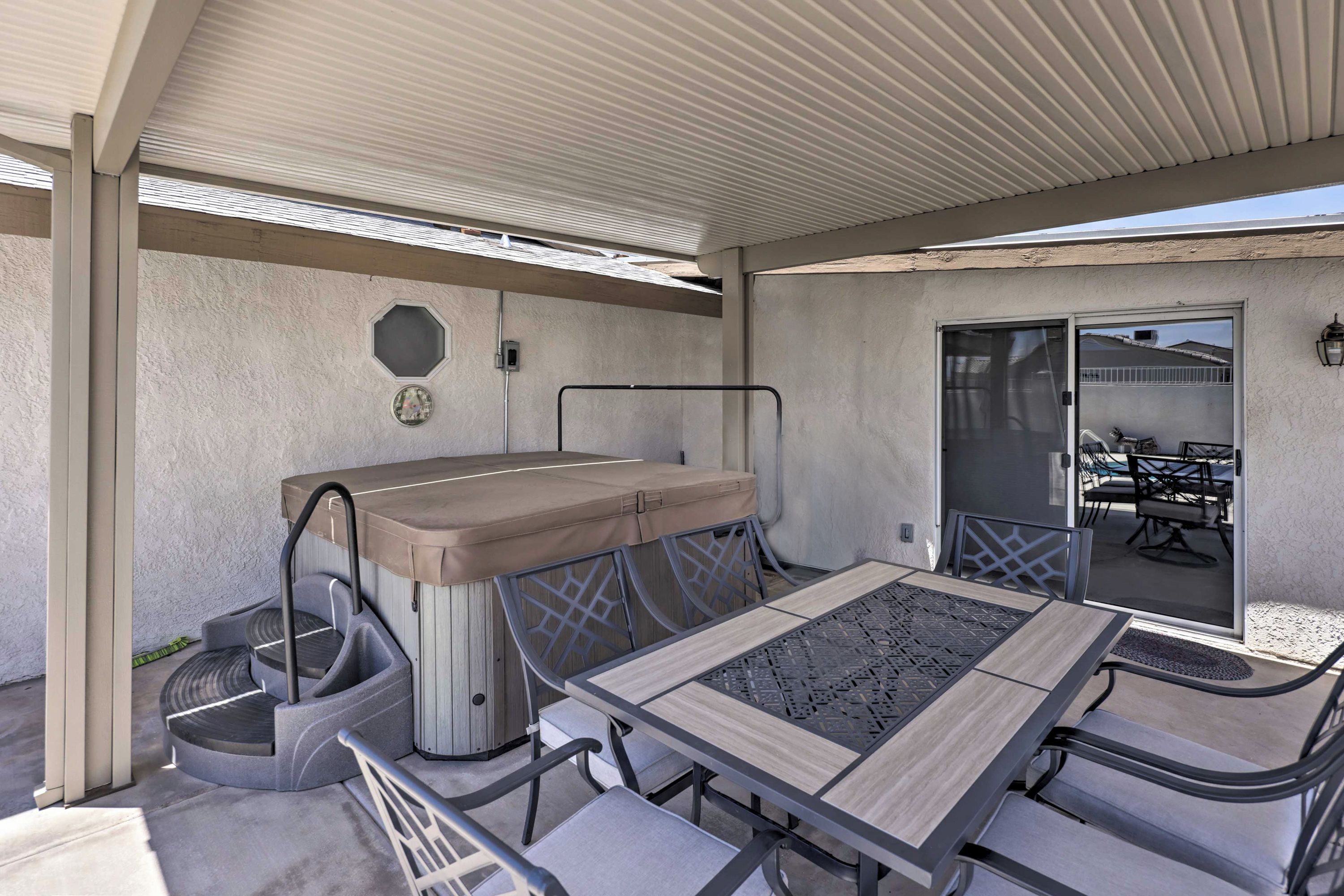 Un patio exterior con mesa y sillas, una zona de estar cubierta y una puerta corrediza que da a otro patio adyacente.