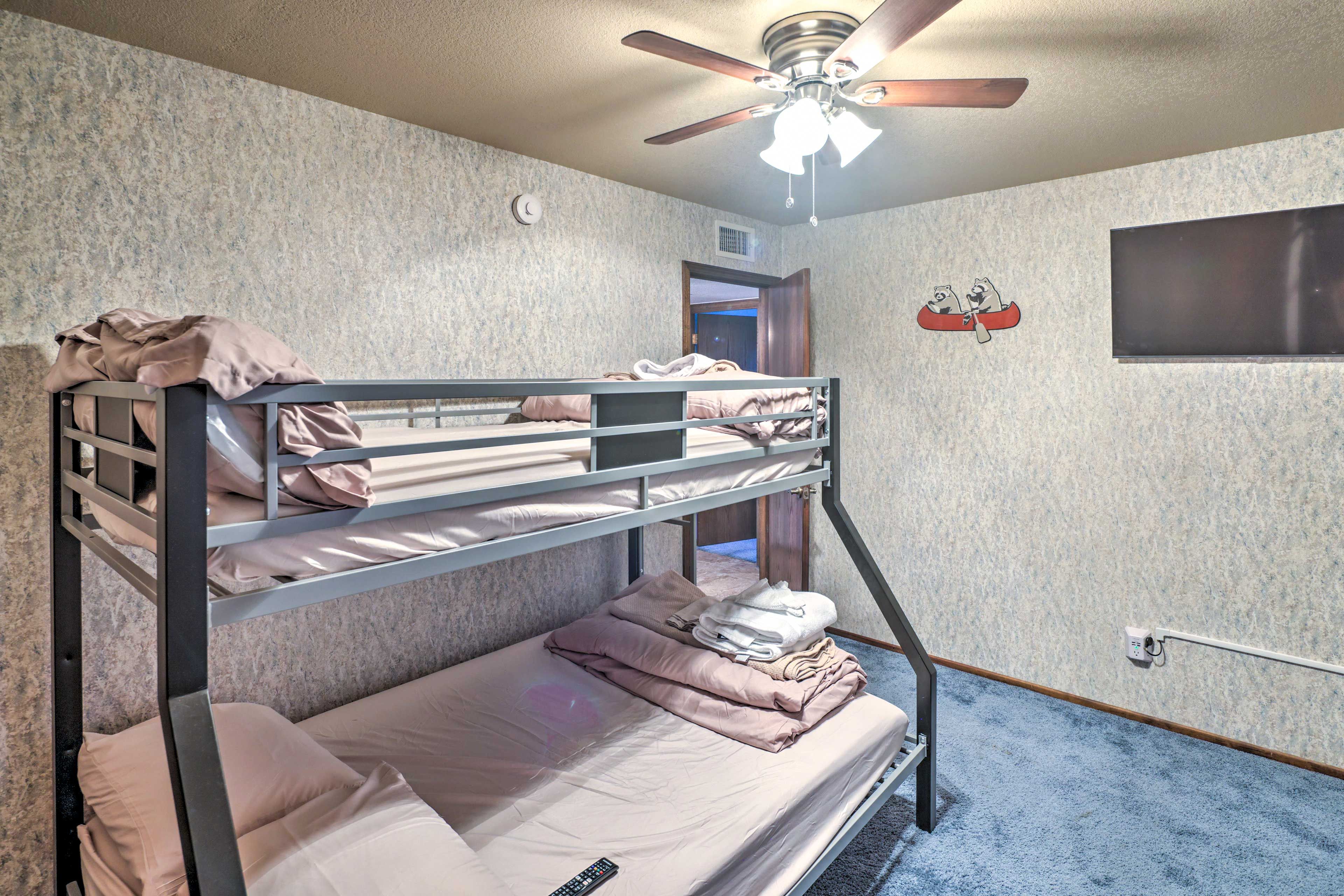 A bunk bed room with a ceiling fan, a wall clock, and a TV mounted on the wall.