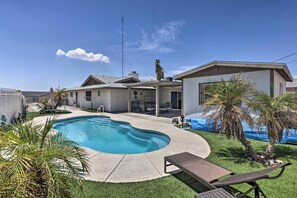 A residential backyard with a swimming pool, a covered patio, and a lawn.