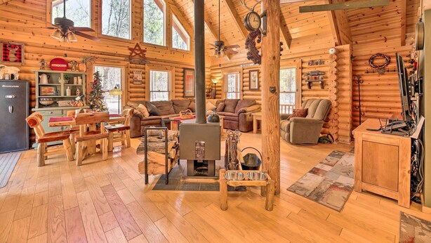 Interior acogedor de una cabaña de troncos con chimenea central, muebles de madera y decoración rústica.