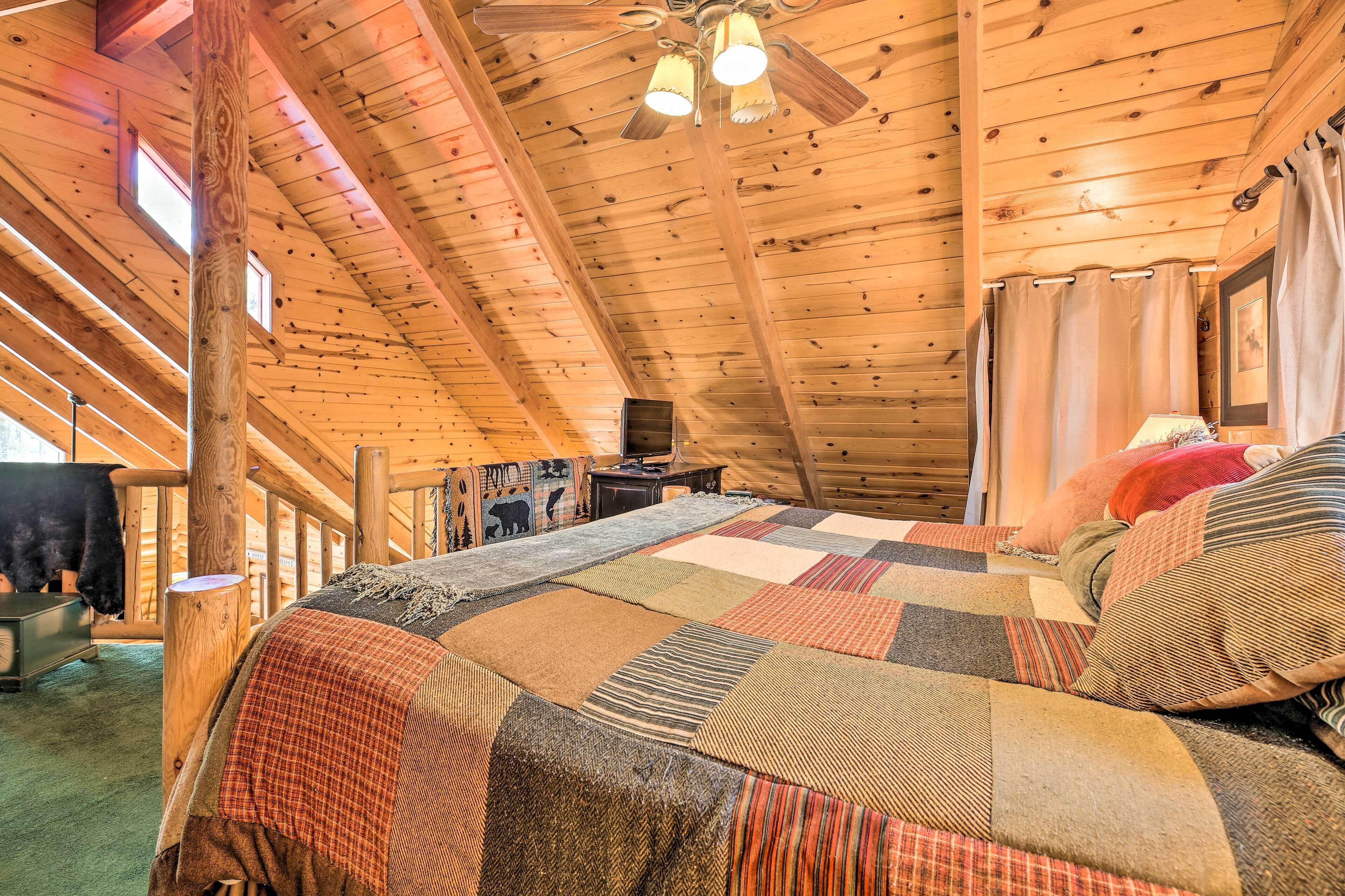 Un dormitorio rústico tipo cabaña de madera con una cama grande, ventilador de techo e interiores de madera.