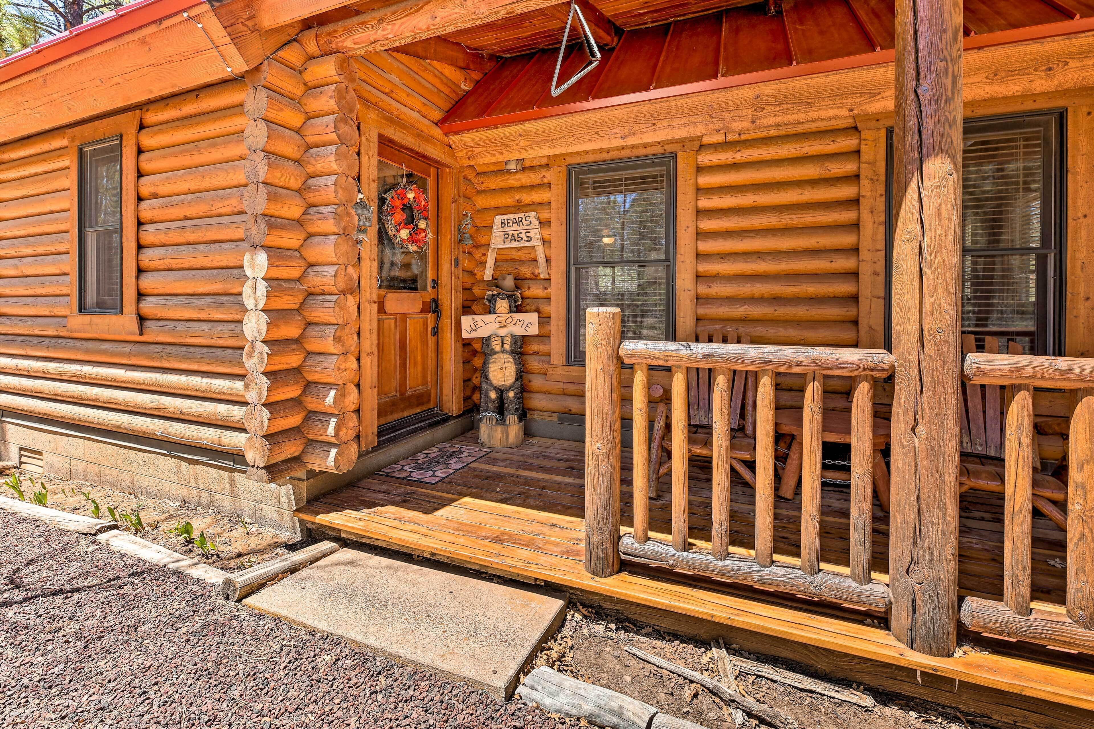 A log cabin with a wooden porch, a welcome sign, and a bear pass sign.